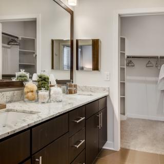 A modern bathroom with a marble countertop and adjacent walk-in closet.
