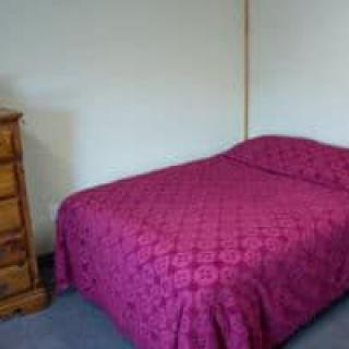 A bedroom with a bed covered in a pink quilt and a wooden dresser.