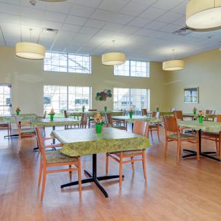 A spacious dining hall with multiple tables and chairs, featuring large windows and modern lighting fixtures.