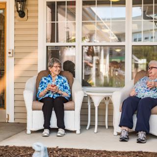 Two elderly individuals sitting and relaxing on a porch during the day.