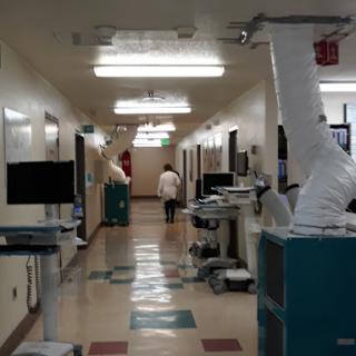 A view of a hospital hallway with medical equipment and a healthcare professional walking in the distance.