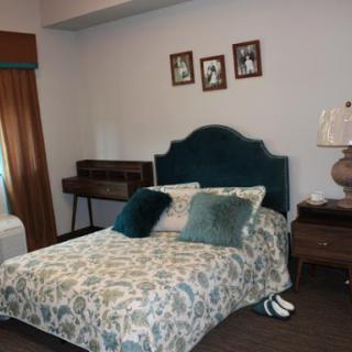 A cozy bedroom featuring a floral-patterned bedspread, plush pillows, and decorative photos on the wall.
