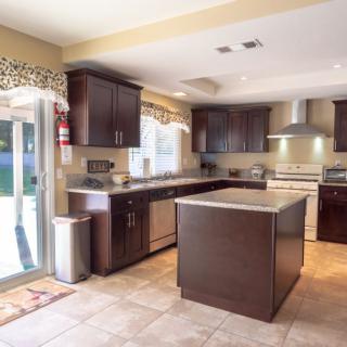 A modern kitchen with dark wood cabinets and a central island, featuring stainless steel appliances and ample natural light.