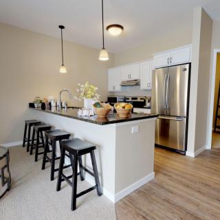 A modern kitchen with an island and stainless steel appliances, featuring pendant lights and bar stools.