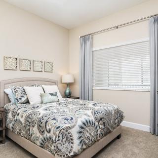 A well-decorated bedroom with a bed, cozy bedding, and a lamp by the window.