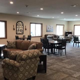 A spacious lounge area with comfortable sofas, tables, and chairs, featuring ample natural light from multiple windows.