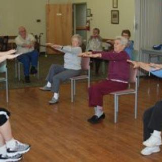 A group of seniors participating in a seated exercise class indoors.