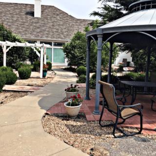 A peaceful garden area featuring a gazebo and outdoor seating surrounded by landscaped paths and potted plants.