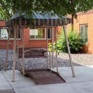 A shaded outdoor swing with a striped canopy in a courtyard setting.