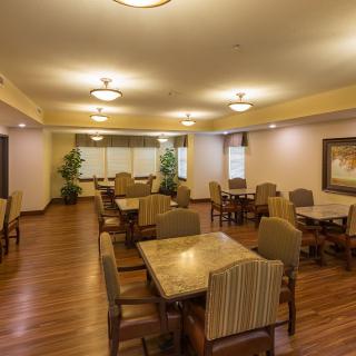 A dining area with neatly arranged tables and chairs, featuring warm lighting and wooden floors.
