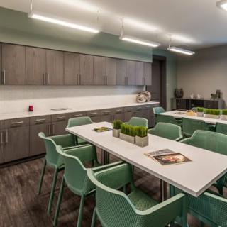 A modern kitchen and meeting area with green chairs and tables, complemented by wooden cabinets and ambient lighting.
