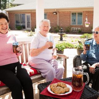 Three seniors enjoying drinks and cookies on a sunny patio.