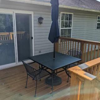 A cozy outdoor dining setup on a wooden deck with a table, chairs, and an umbrella.