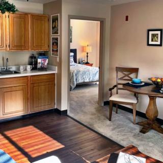 A cozy apartment interior featuring a compact kitchen, dining table, and a glimpse into the bedroom.