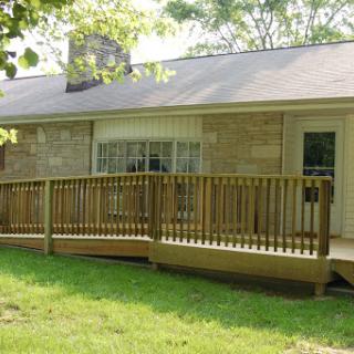 A cozy house featuring a wooden deck that extends into the grassy yard.