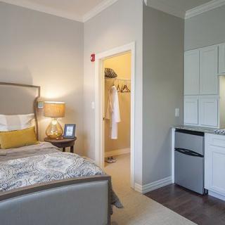 A modern bedroom with a bed, adjacent closet, and kitchenette area.