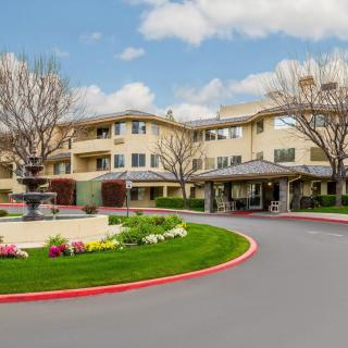 A beautifully landscaped residential building with a driveway and fountain on a cloudy day.