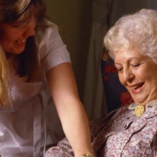 A caregiver assisting an elderly woman with a warm smile.