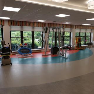 A bright and spacious rehabilitation therapy room equipped with various exercise machines and colorful flooring.