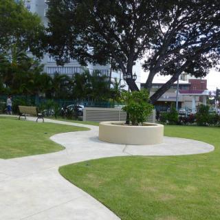 A tranquil park with a winding pathway and benches beneath large trees.