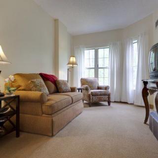 A cozy living room with a sofa and armchair, featuring soft lighting from table lamps and natural light through the windows.