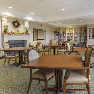 A cozy dining area with tables, chairs, a fireplace, and a bookshelf.
