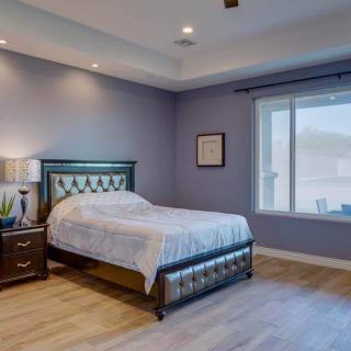 A modern bedroom with a blue color scheme, featuring a bed, nightstand, and large window.