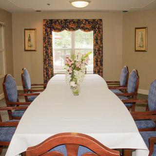 A neatly arranged dining room with a long table and chairs, featuring decorative curtains and a flower centerpiece.