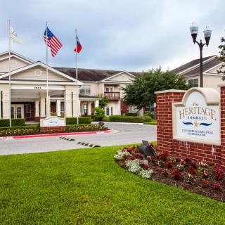 A hotel entrance with well-maintained landscaping and flags, set against a cloudy sky.