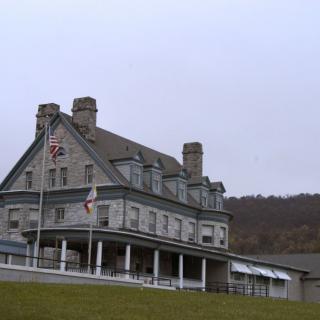 A historic building with flags and a large porch set against a cloudy sky.
