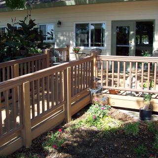 A house with a wooden ramp and railing leading to a garden area.