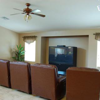 A cozy living room set up as a home theater with leather chairs facing a large TV.