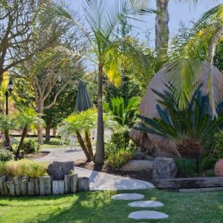 A serene garden landscape featuring a winding pathway, lush greenery, and large boulders.