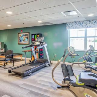 A well-lit indoor gym featuring exercise equipment including a treadmill and stationary bikes.