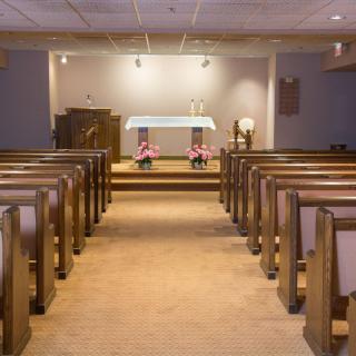 A serene chapel interior with rows of pews leading towards an altar adorned with flowers.