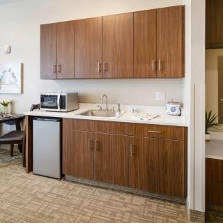 A modern kitchenette with wooden cabinets, a stainless steel refrigerator, and a microwave.