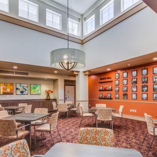 A modern dining area with a high ceiling, featuring multiple seating arrangements and decorative artwork on the walls.