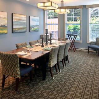 A well-decorated dining room with a large table and chairs, featuring artwork on the walls and ample natural light from the windows.