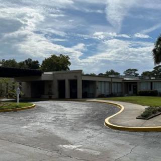 A modern building with a curved driveway under a partly cloudy sky.