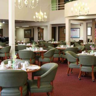 A spacious dining room with elegant chandeliers, neatly arranged tables, and comfortable green chairs.
