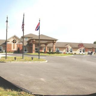 A single-story building with multiple flags in front, surrounded by a parking lot under clear skies.