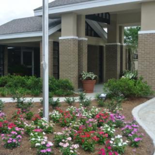 A building entrance with a landscaped garden featuring colorful flowers and a flagpole.