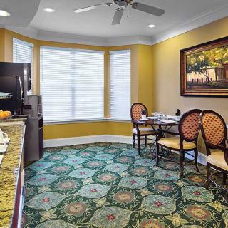 A cozy dining area with patterned carpet, a small table and chairs, and a large window.