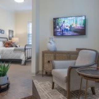 A cozy living space featuring a comfortable chair, a wall-mounted TV, and a stylish transition into the bedroom.