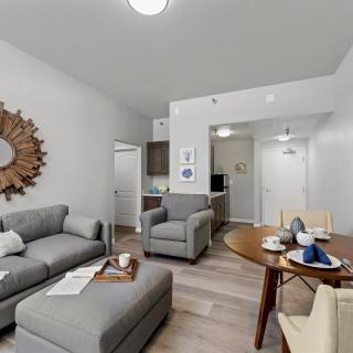 A modern living room with a comfortable sofa and armchair, alongside a dining area with a wooden table.
