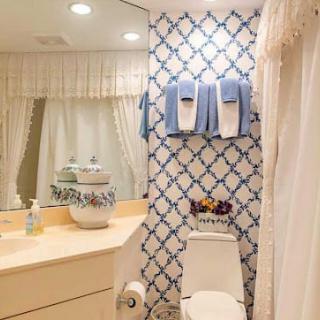 A cozy bathroom with patterned wallpaper, neatly arranged towels, and a well-lit vanity area.