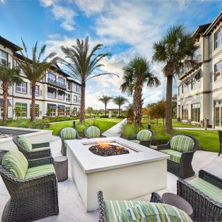 A modern residential complex features a cozy outdoor seating area with a fire pit surrounded by palm trees.