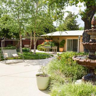 A serene garden patio with a fountain, surrounded by lush greenery and outdoor seating.