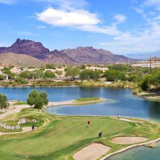 A scenic view of a golf course with a lake and mountains in the background.