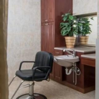 A hair salon station featuring a black barber chair, a sink, and a large mirror with potted plants.